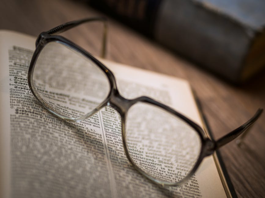A pair of glasses with square-shaped frames on a book.