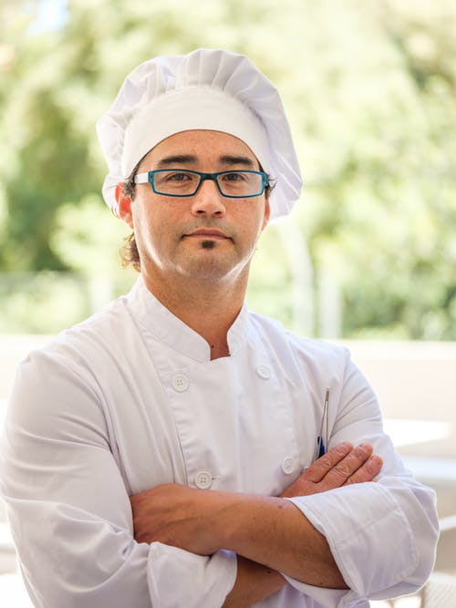 A man wearing chef's whites wearing flat top-style glasses.